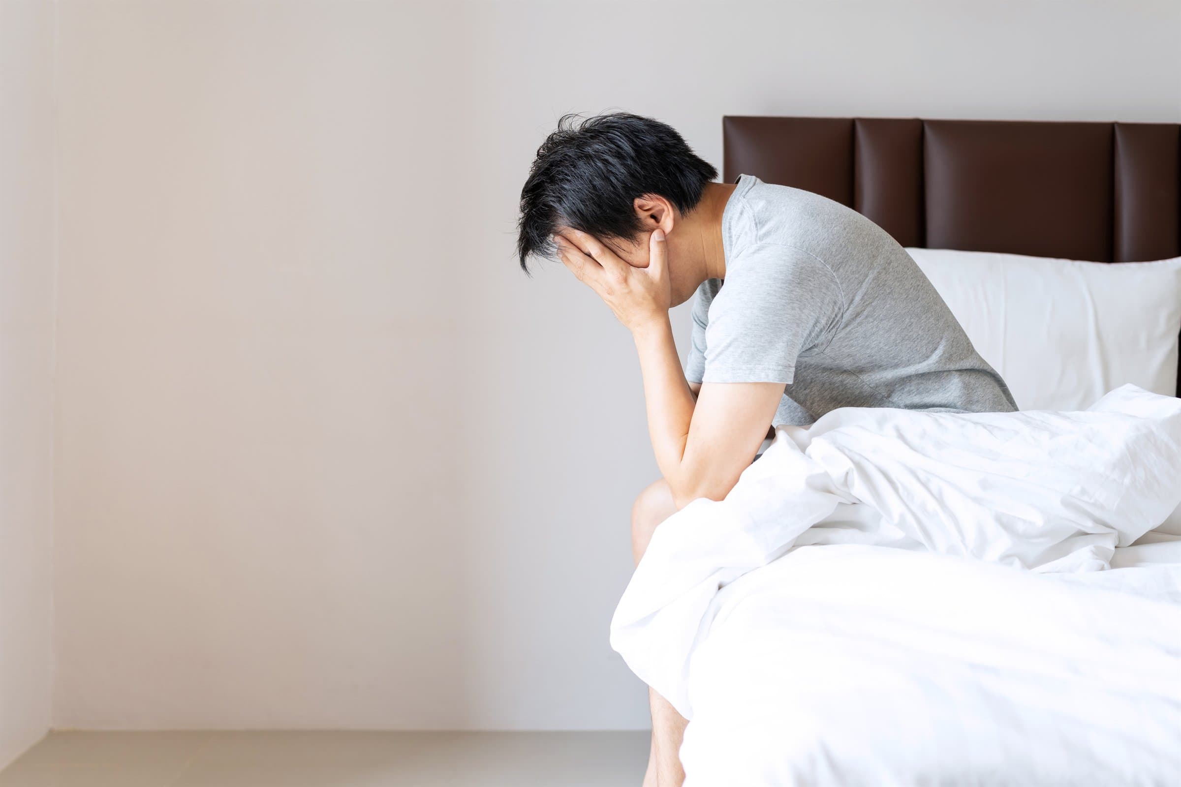 ベッドに腰かけて悩む男性